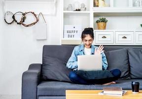 una adolescente asiática está sentada en el sofá de su propia casa hablando con sus colegas sobre un proyecto de trabajo en una computadora sobre su trabajo en la empresa foto