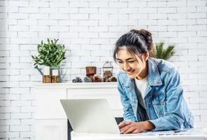 Young smiling happy asian woman relaxing connected on internet with laptop computer working and video conference meeting at home.Young creative typing on keyboard, work from home concept photo