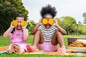 Two African American little girl sitting on the mat and eating oranges fruits in the autumn park , play with oranges fruits photo