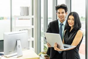 Asian Businessman and businesswoman holding a laptop computer were discussing jobs while standing in office building windows overlooking the city photo