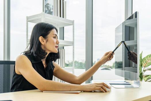 retrato de una mujer de negocios asiática señalando con un bolígrafo y pensando en un tema mientras está sentada en la oficina con su computadora foto