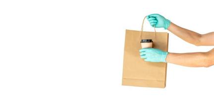 Delivery man hand in sterile gloves holding food in craft paper bag  and coffee isolated on white background with copy space, safe delivery during a virus quarantine pandemic, stay home. photo