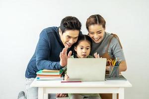 Happy young mother and father and little daughter making video call with laptop computer, gesturing hi, having conversation with  grandfather or grandma using wireless internet connection photo