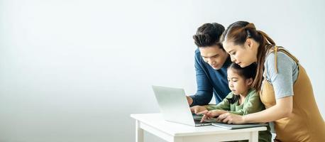 Happy young Asian family using at the laptop to surf internet together at home, , relaxing at home for lifestyle concept