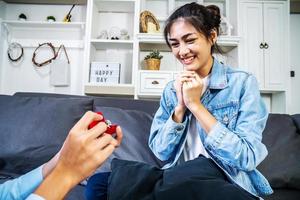 ¿Quieres casarte conmigo, un joven que le da un anillo de compromiso en una pequeña caja roja a su hermosa y feliz novia en casa? hombre haciendo propuesta de matrimonio a su amada mujer. cita romántica. foto