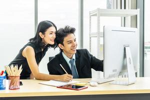 We already have great results, Young business man pointing at laptop computer with smile and discussing something with her coworker while standing at office photo