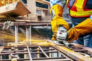 Young man welder in a working blue overall and working gloves grinds a metal object with a angle grinder in the garage, bright sparks fly to the sides photo