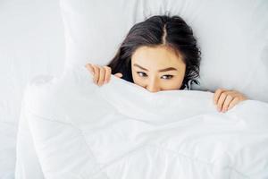 Wake up. Lonely Beautiful young asian woman waking up after good night sleep, in the morning in bed covering her face under blanket, View from above, Copy space. photo