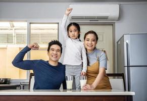 Happy family having fun in the kitchen. Asian Father, mother and little daughter spending time together and having breakfast drinking and hold glasses of milk at table photo