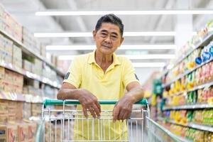 Asian senior man shopping trolley choosing other products in supermarket photo