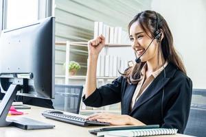 Smiling beautiful businesswoman with headset working in call center as a customer service agent celebrating a good job in the workplace photo