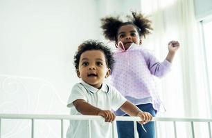 Happy African American naughty kids boy and girl jumping on the bed with happiness.two funny small energetic mixed race children brother with sister having fun play on bed