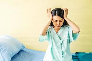 pacientes asiáticas jóvenes que sufren dolor de cabeza con las manos en la frente. concepto médico y sanitario. mujer enferma con el ceño fruncido sentada en la cama en la habitación del hospital. foto