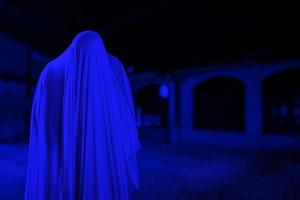 el hombre está vestido de blanco y muestra una cara aterradora en un edificio antiguo y espeluznante, parece un fantasma en la noche para el concepto del festival de halloween, copia espacio foto