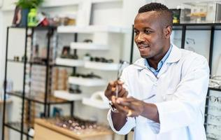 Eyesight And Vision Concept. Portrait of smiling african american standing at optics store and pointing at showcase and rack with many eyewear and specs frames. Guy offering spectacles photo