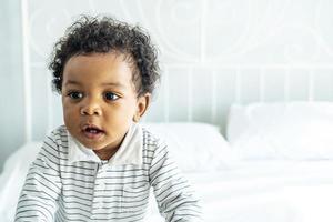 Adorable african baby with fluffy hair standing on the bed, Pretty boy photo