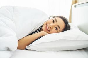 Young beautiful woman smiling while lying on white pillow in bed at early morning photo