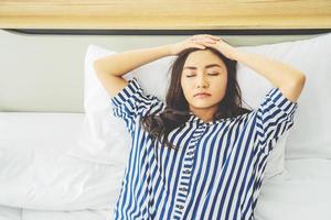 una joven asiática infeliz y pensativa tocándose la frente, sintiéndose triste y solitaria acostada en la cama sola tratando de dormir pensando en problemas, miedos, preocupaciones y desesperanza.