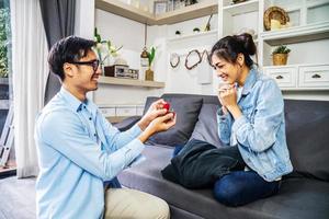 ¿Quieres casarte conmigo, un joven que le da un anillo de compromiso en una pequeña caja roja a su hermosa y feliz novia en casa? hombre haciendo propuesta de matrimonio a su amada mujer. cita romántica. foto