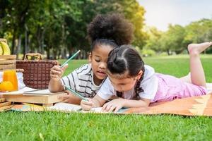 Two american african little girl lying and drawing with colored pencils at summer park, feel happiness, outdoor education concepts photo