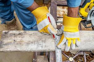 Construction worker wears protective leather gloves, with a pencil and the carpenter's square trace the cutting line on a wooden table. Construction industry, housework do it yourself. photo