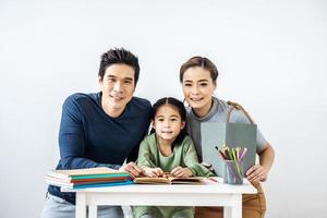 retrato disfrute feliz amor sonriente familia asiática padre y madre ayudando a la pequeña hija a hacer la tarea en casa en la sala de estudio, concepto de educación foto