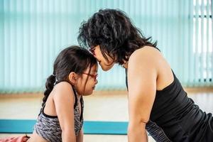 Asian fit mother with little child daughter are smiling while practicing yoga together at home, exercise class on asana mat at home. parent accompany healthy children sport concept photo