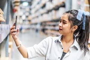 joven asiática escaneando el código qr a través de un teléfono móvil inteligente para comprobar el stock y el precio de los productos en el almacén, las compras de los clientes y el autoservicio, el concepto de tecnología moderna foto