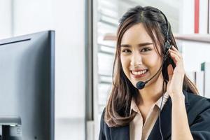 Smiling friendly asian female call-center agent with headset working on support hotline in the office photo