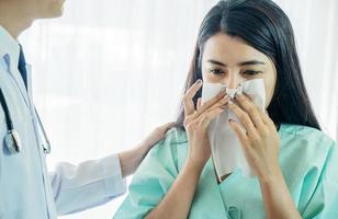 Primary care doctor making diagnosis to sick woman, unhappy patient using a tissue to sneeze and blowing her nose and get high fever from flu and cold, Patient care and healthcare. photo