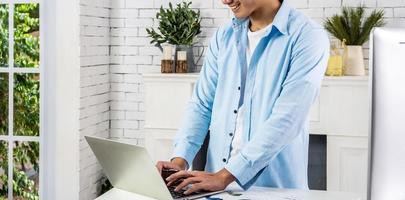 Young smiling happy asian man relaxing connected on internet with laptop computer working and video conference meeting at home.Young creative typing on keyboard.work from home photo
