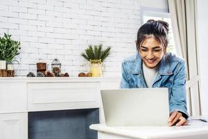 Young smiling happy asian woman relaxing connected on internet with laptop computer working and video conference meeting at home.Young creative typing on keyboard, work from home concept photo