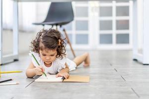 Cute Little girl writing on a notebook lying floor, learning concept at home photo