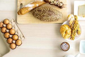 Fresh homemade baked bread with butter served as breakfast on white table with boiled eggs and milk coffee on wooden table. Top view with copy space photo