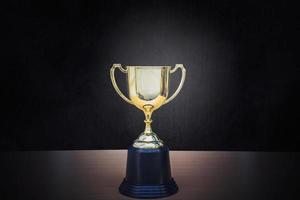 Golden trophy placed on top of old wooden table in front of dark background copy space ready for your design win concept. photo