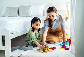 Happy asian mother and asian baby girl playing educational toys on the floor in the bedroom. Home activities for family. photo