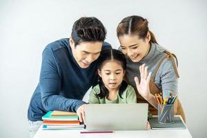 feliz joven madre y padre e hija pequeña haciendo videollamadas con una computadora portátil, saludando, conversando con el abuelo o la abuela usando una conexión inalámbrica a internet foto