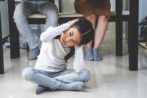 hijita asiática triste y tapa los oídos debajo de la mesa mientras los padres pelean en la cocina, diseño de fotos para problemas familiares y concepto infeliz