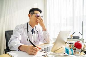 Troubled asian man doctor working on computer at desk in hospital clinic, worried, thinking hard, healthcare concept for Covid19. photo