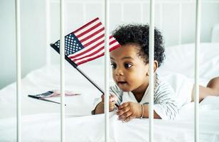 Cute Baby Boy afroamericano sosteniendo la bandera americana en la cama foto