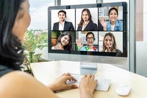 Business woman sit at desk looking at computer screen where collage of diverse people webcam view. Asian woman lead video call distant chat, group of different mates using video conference photo