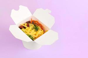 wok de arroz con mariscos y verduras en una caja blanca aislada de fondo morado, comida para llevar foto