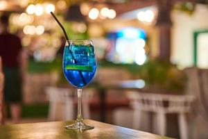 Blue Lagoon cocktail drink in glass with straw, night cafe light bokeh background copy space photo