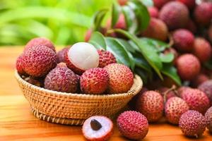 fruta de lichi en una cesta con hojas verdes y fondo de madera, lichi fresco y maduro pelado del árbol de lichi en la fruta tropical tailandia en verano foto