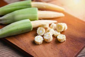 Baby corn on wooden cutting board, Fresh young baby corn for cooking health food, Close up raw organic baby corn on wooden background. photo