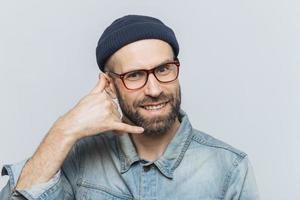 Call me please. Happy handsome man holds hand near ear, imitates mobile phone conversation, smiles joyfully, waits for call from someone, isolated over grey studio background. Communication concept photo