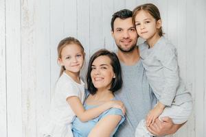 Good looking female and male parents hold their beautiful daughters, spend free time all together, enjoy togetherness. European family love each other, have fun. People, family, relations concept photo