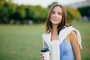 People, recreation and lifestyle concept. Beautiful young European woman has serious look at camera, dressed casually, spends free time at nature, drinks hot beverage, enjoys rest, peaceful atmosphere photo