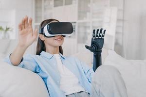 Psychological rehabilitation for handicapped. Happy girl with artificial robotic arm in vr glasses. photo