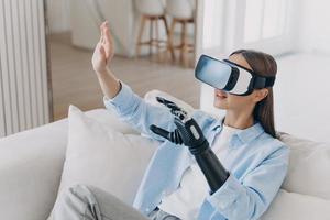 European handicapped girl in vr glasses on sofa at home. Healing technology, robotic limb. photo